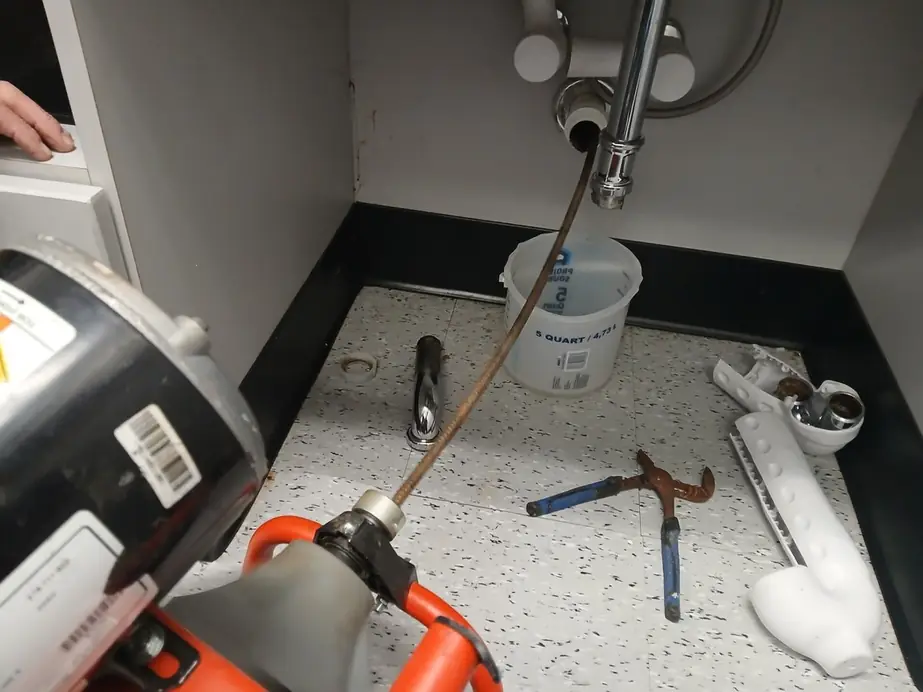 Garbage disposal mounted under a kitchen sink, tools on the counter above